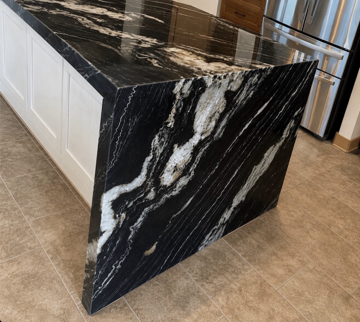 Black granite island with white and gold veining, a waterfall panel and a 2½-inch wrapped mitered edge