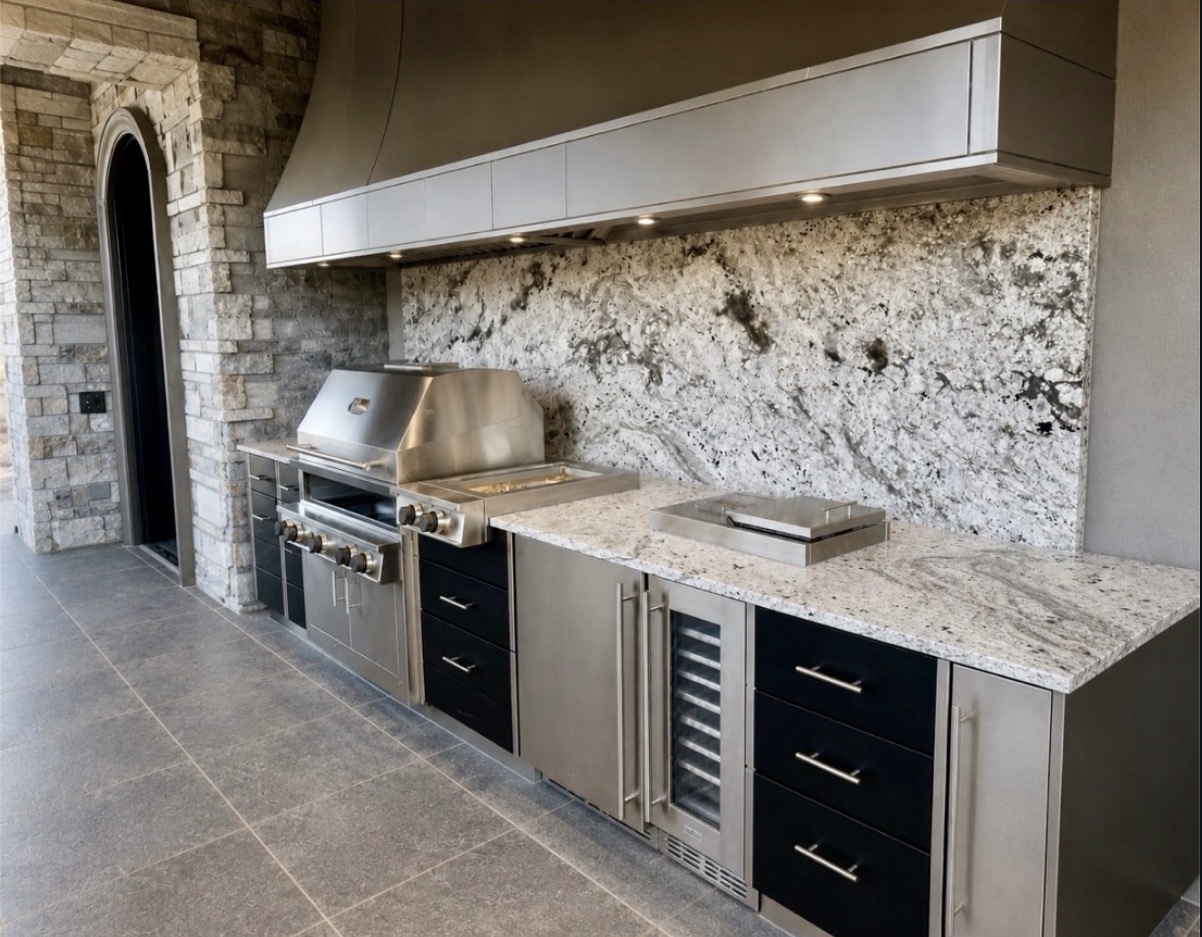 Outdoor kitchen with stone countertops and a full-height stone backsplash, stainless steel grill, broad hood and beverage cooler