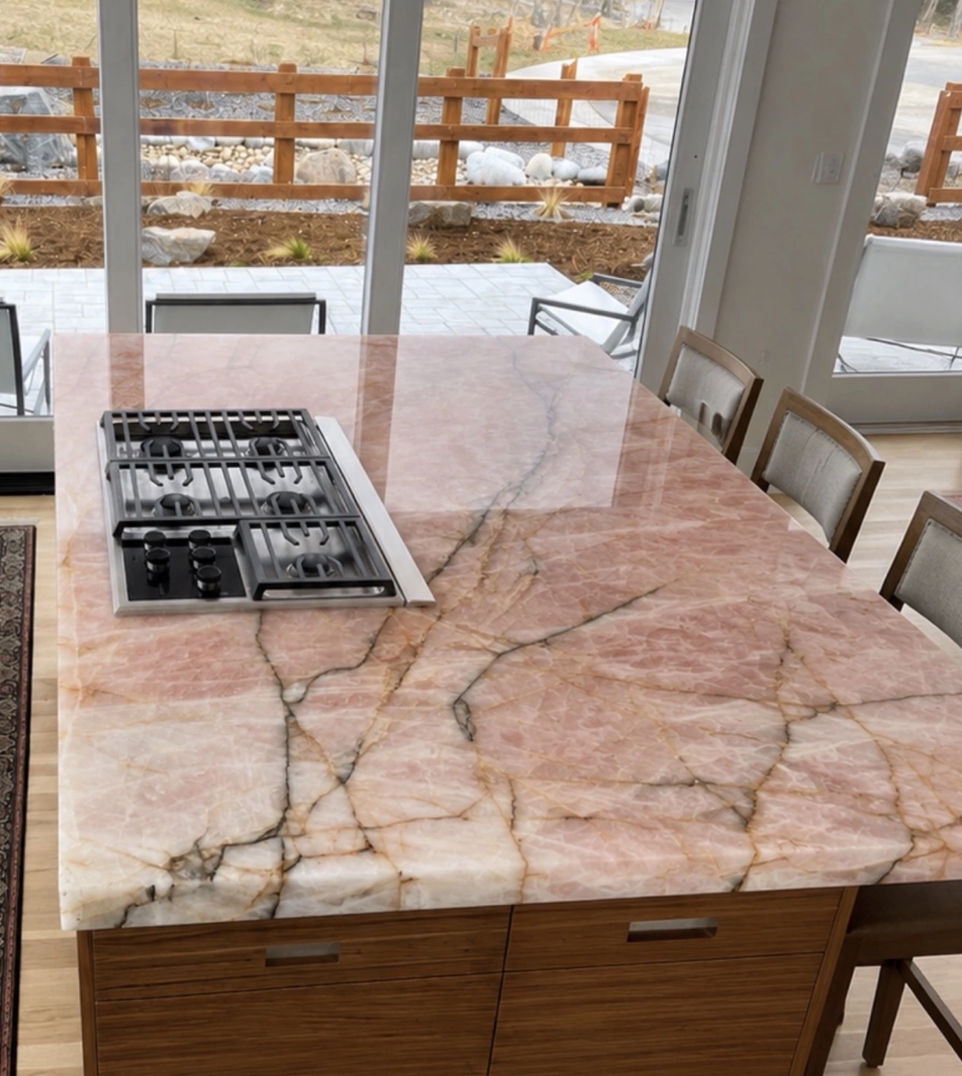 Final result: installed pink and white veined stone kitchen island with a built-in cooktop and wood cabinetry