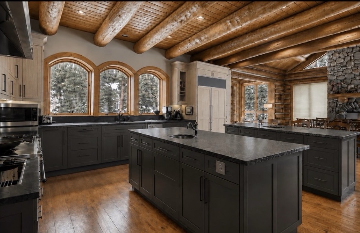 Dark quartz countertops with chiseled edges on a kitchen island and perimeter cabinets, beneath a timber ceiling with arched windows