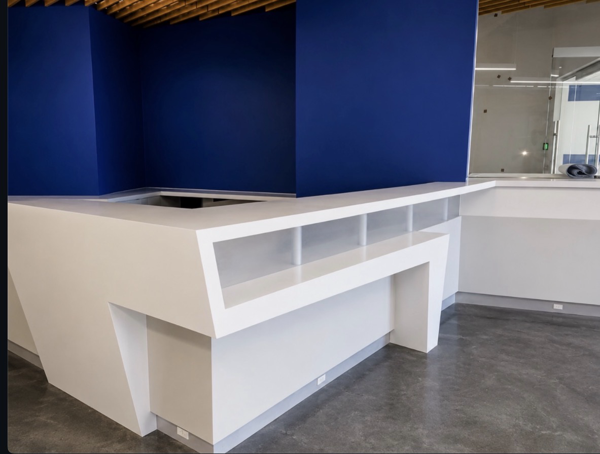 White quartz reception counter with geometric framing and recessed display shelves against deep blue walls