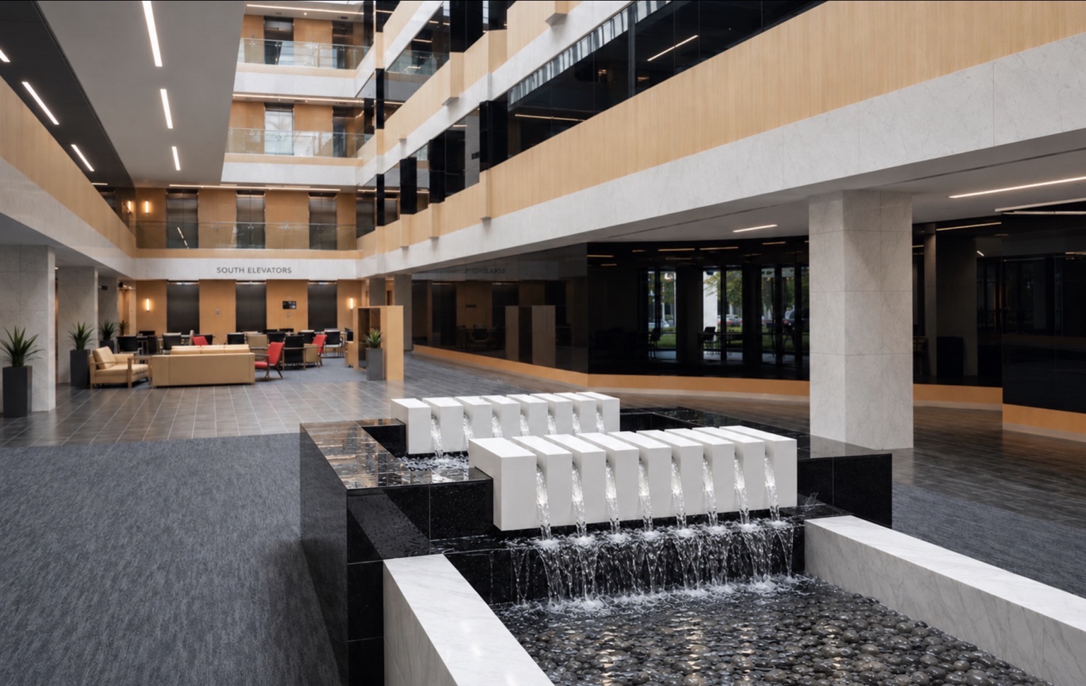 White quartz waterfall fixtures cascading into a black stone fountain basin in a commercial atrium