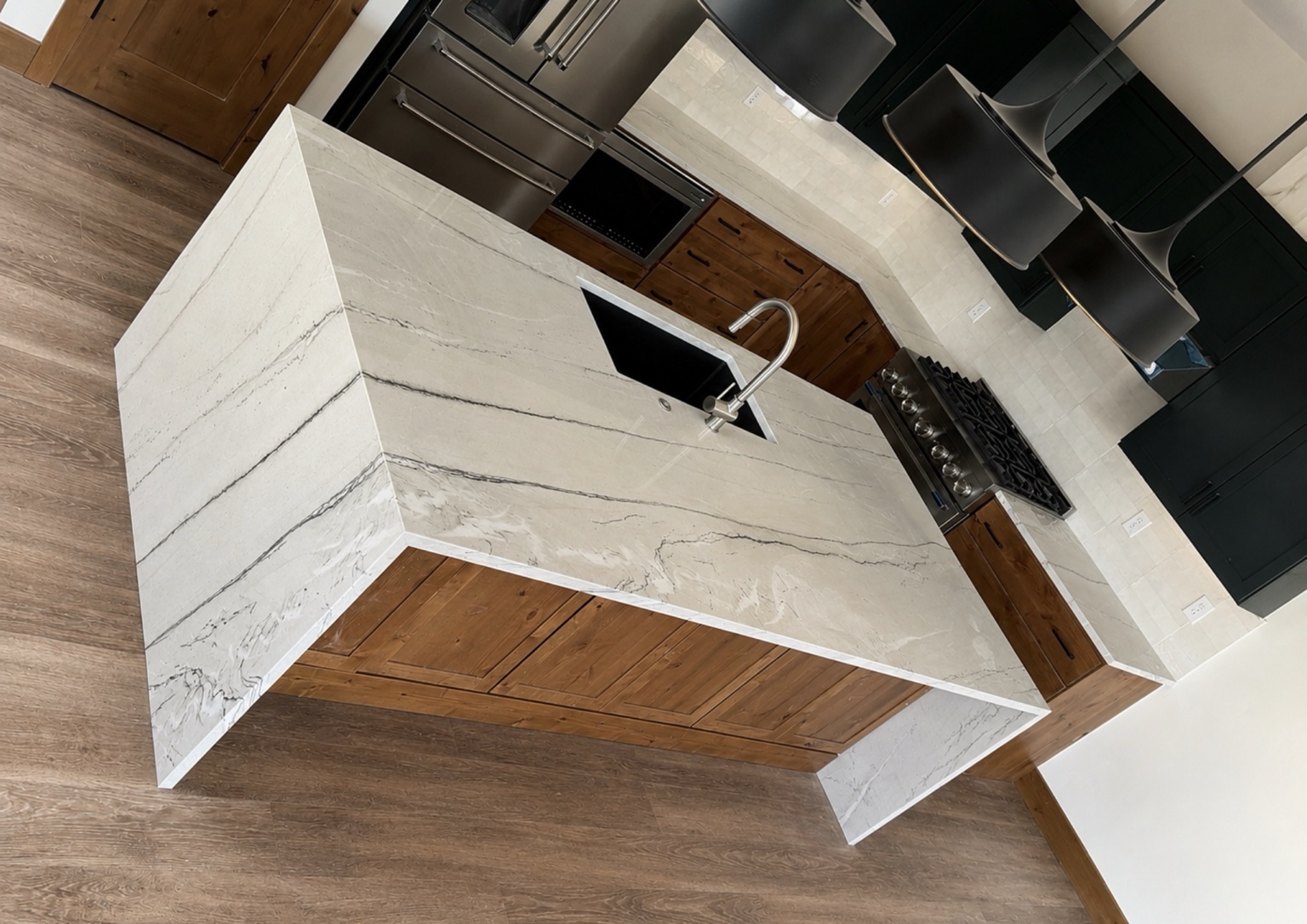 Ivory quartzite kitchen island with gray veining, waterfall panels on both ends, mitered corners, wood cabinetry and a black undermount sink