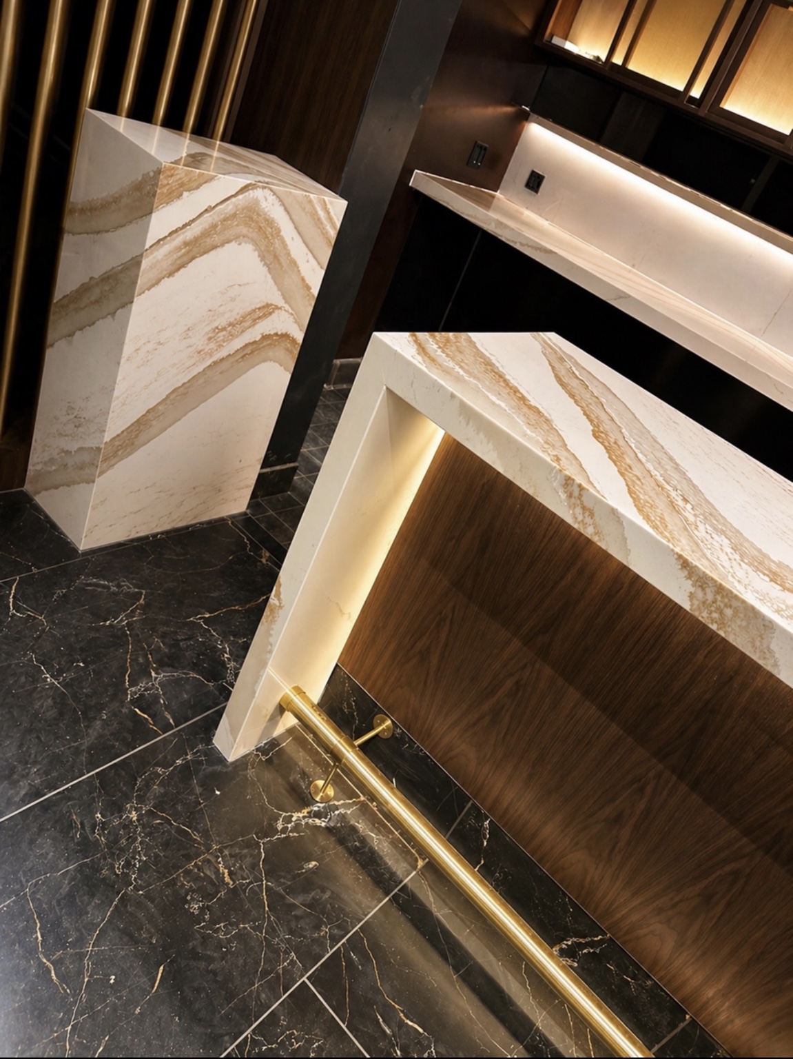 Gold-toned veining continuing from a pale bar countertop down mitered waterfall panels beside warm wood cabinetry and brass accents